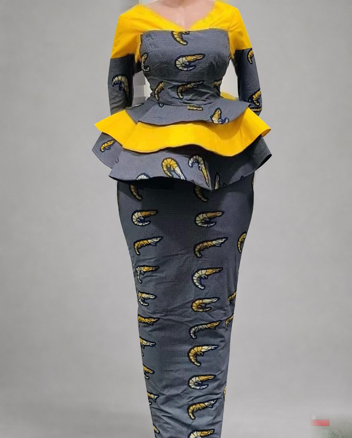 TL-branded background-edited photograph against a neutral grey studio background: a mannequin displaying a yellow and grey patterned outfit with layered peplum and long skirt