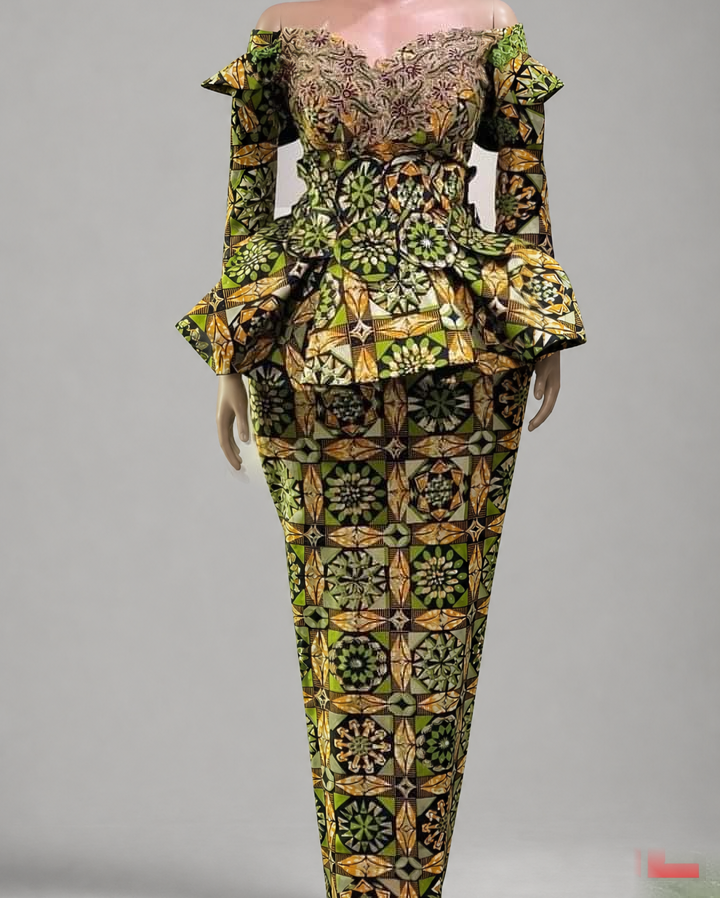 TL-branded background-edited photograph against a neutral grey studio background: a mannequin displaying a green, gold and black geometric-print fashion design with lace neckline and peplum